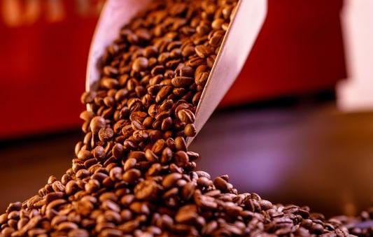 Auf dem Bild sind Kaffeebohnen in einer Schaufel zu sehen, die langsam von der Schaufel rieseln.